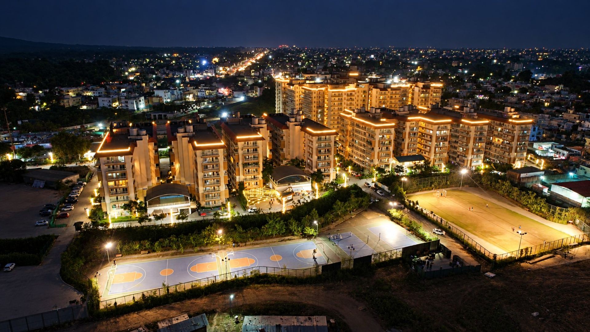 Aerial night view of River Valley Township, Dehradun: lit residential towers, basketball and tennis courts and the football ground